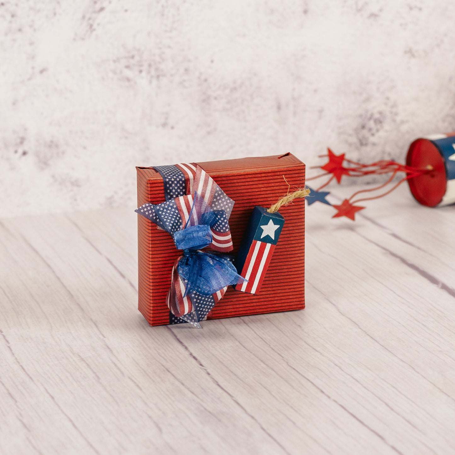 a sampler box of assorted chocolates is wrapped and topped with a wooden firecracker decoration
