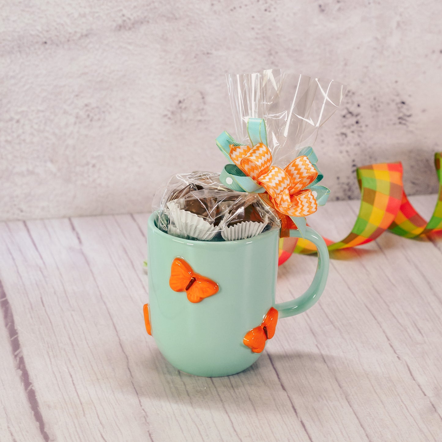 a turquoise mug with 3D orange butterflies over it is filled with a half pound of milk assorted chocolates