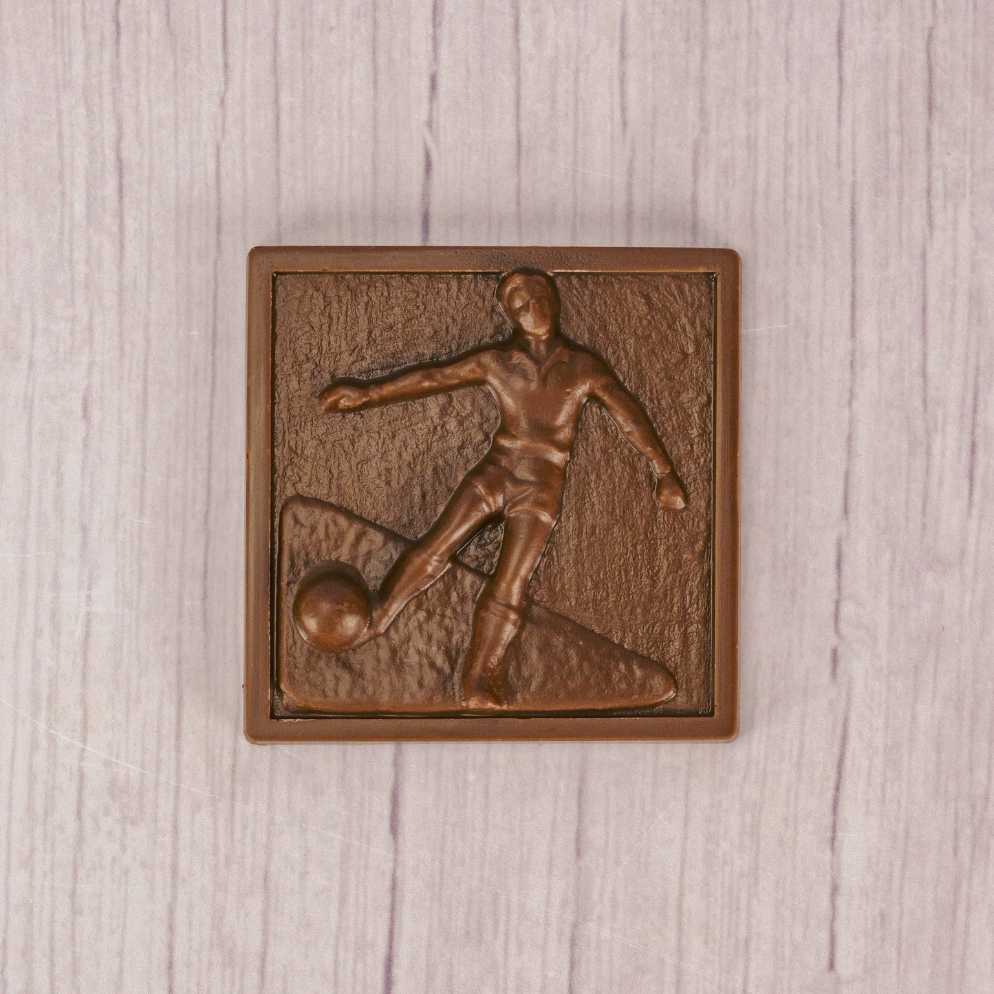 a square plaque of a soccer player kicking the ball in smooth milk chocolate