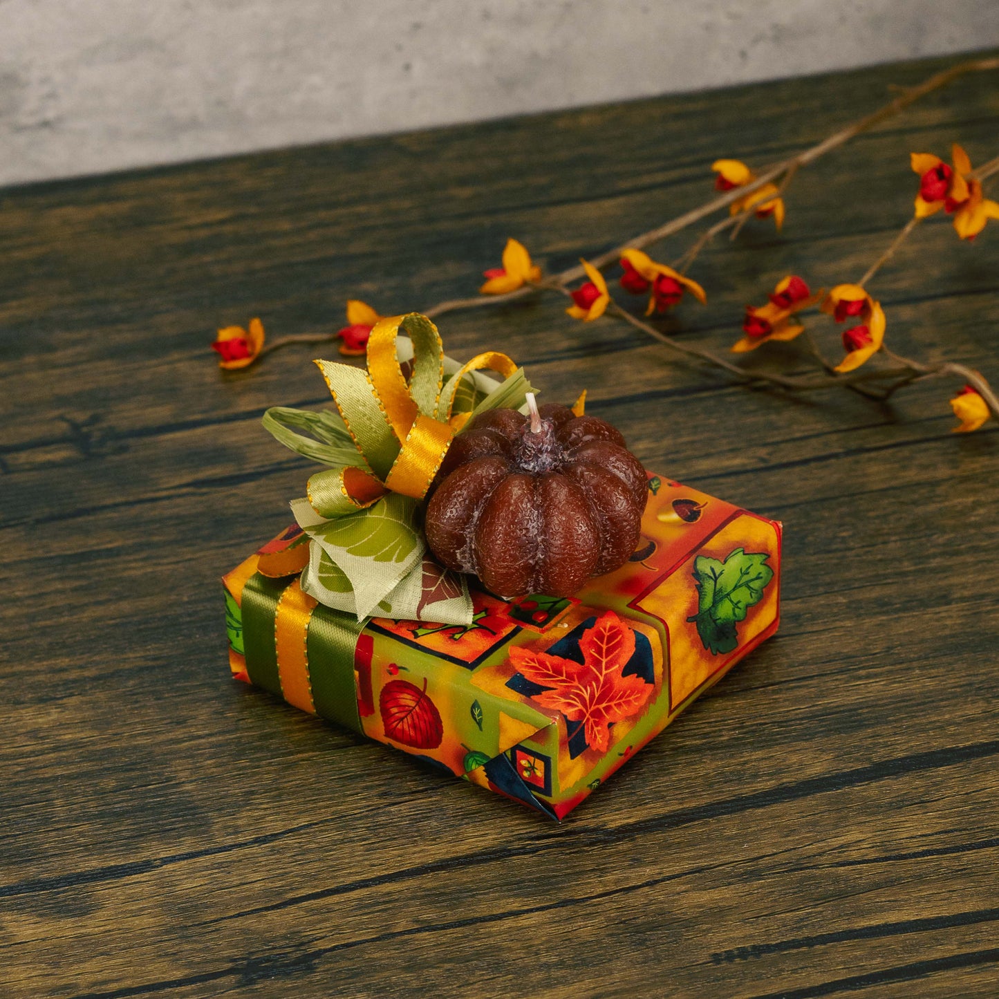a sampler box of assorted chocolates is wrapped in festive fall paper and tied with a lovely handmade bow and topped with a petite pumpkin candle