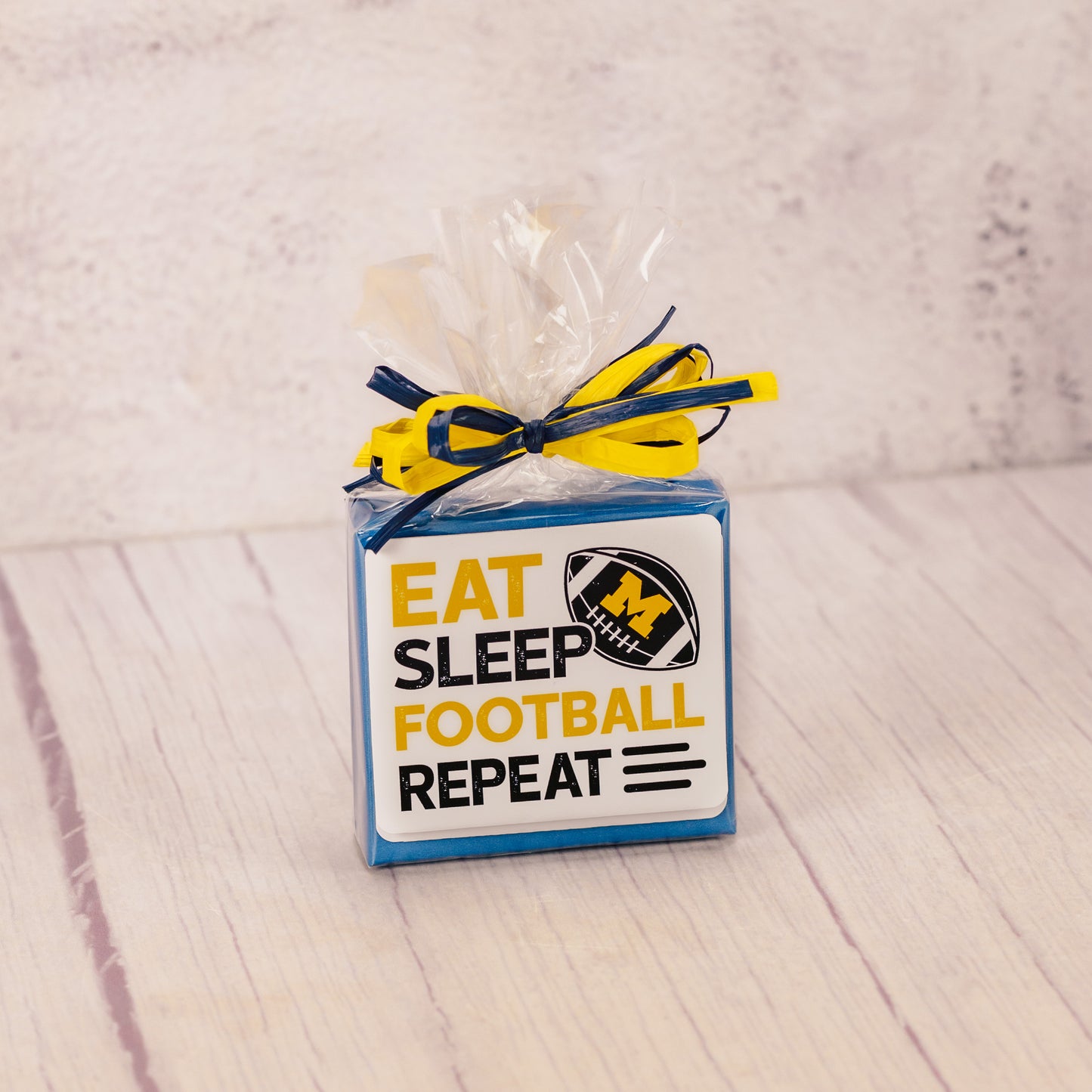 a sampler box of assorted chocolates wrapped and topped with a Michigan football sticker that reads 'eat, sleep, football, repeat'
