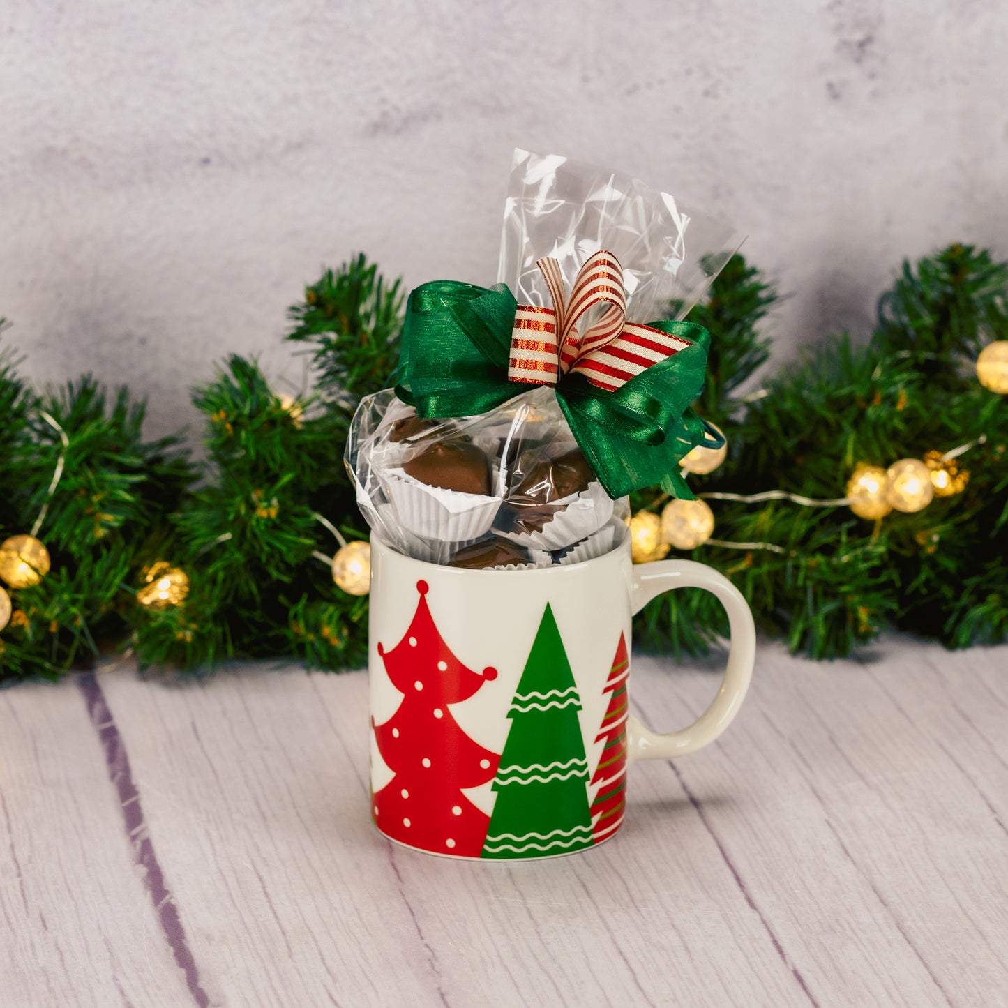 a festive mug that features red and green trees all around the mug is filled with a half pound of our assorted milk chocolates