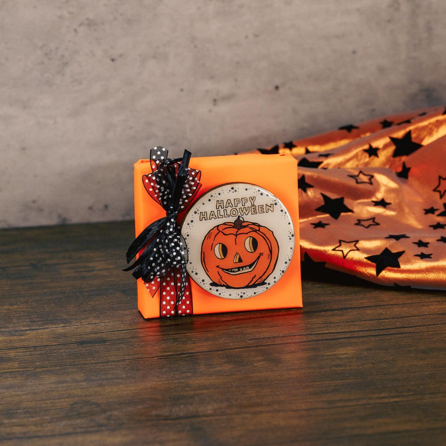 a round wooden jack-o-lantern Halloween magnet, that reads 'happy halloween' is placed on a sampler box of assorted chocolates.