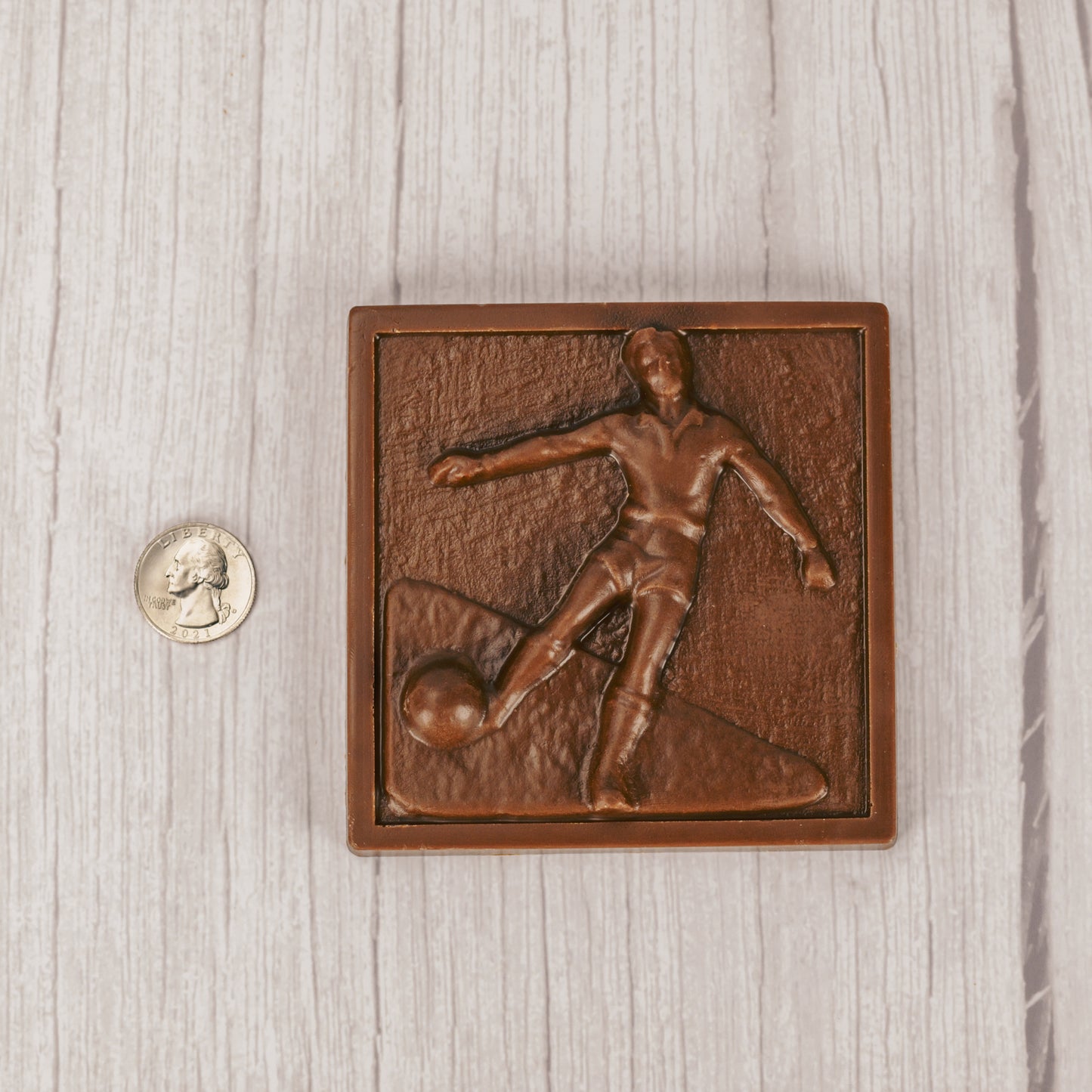 a square plaque of a soccer player kicking the ball in smooth milk chocolate