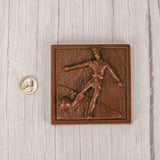 a square plaque of a soccer player kicking the ball in smooth milk chocolate