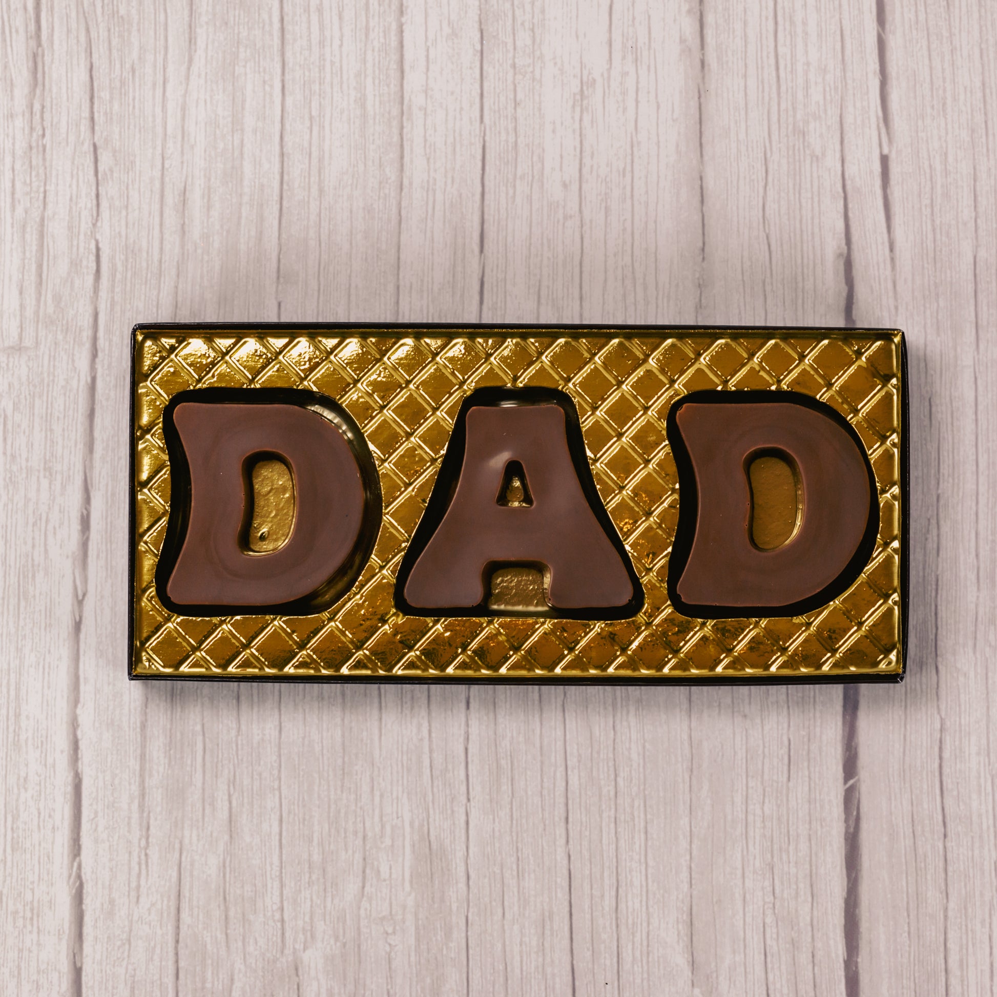 Milk chocolate letters spell out D.A.D and are placed in a box with a clear lid.