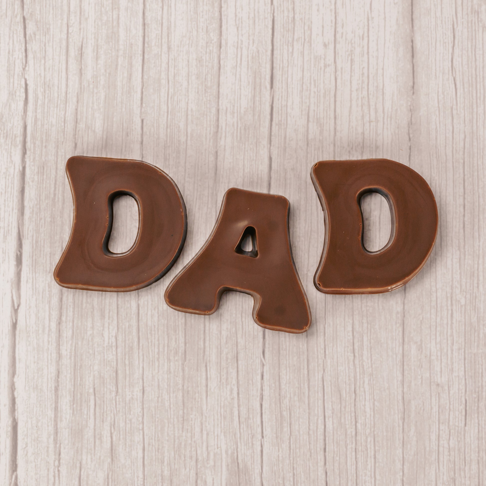 Milk chocolate letters spell out D.A.D and are placed in a box with a clear lid.