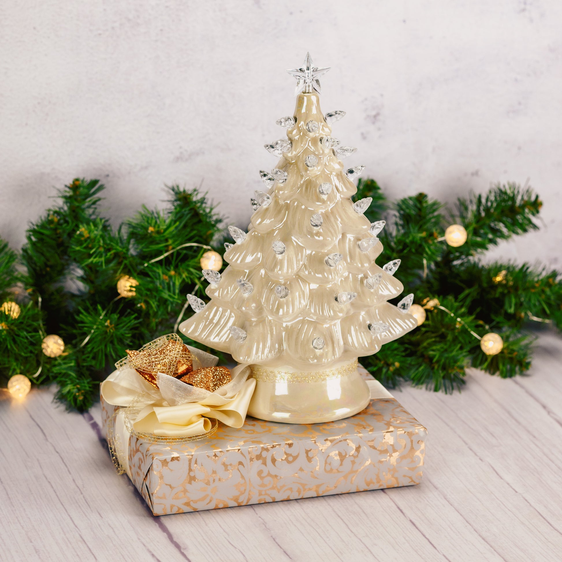 An 8 inch gold pearlescent lighted ceramic tree sits atop a box wrapped in gold filagree paper and tied with a gorgeous handmade bow.
