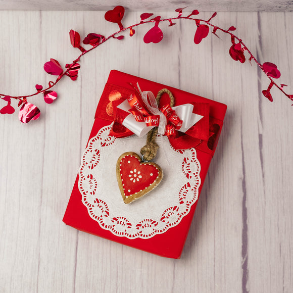 a half pound box of assorted chocolates is wrapped and topped with a wooden heart ornament