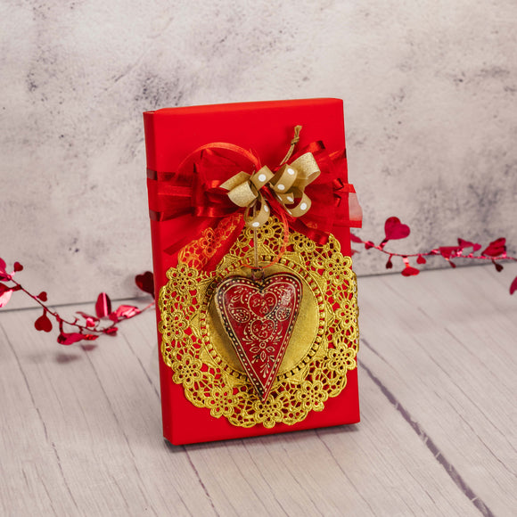 a one pound box of assorted chocolates is wrapped in red and topped with a tin heart ornament 