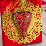 a one pound box of assorted chocolates is wrapped in red and topped with a tin heart ornament 