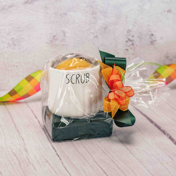 a sampler box of assorted chocolates and a lily pad are packaged with a white ceramic kitchen scrubbie holder and yellow scrubbie