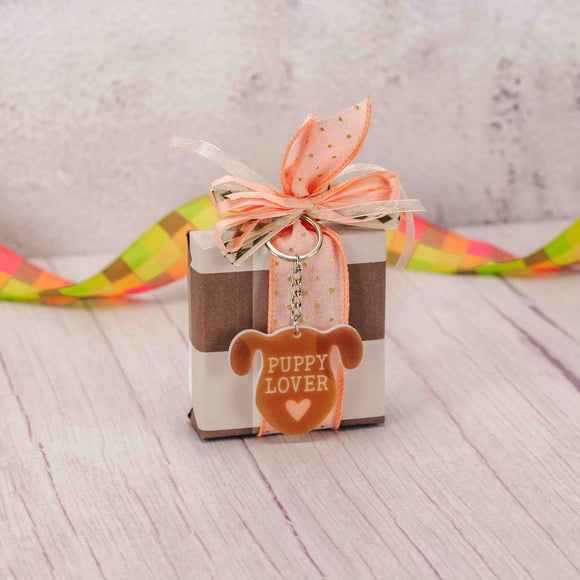 a sampler box of assorted chocolates is topped with an acrylic puppy keychain that reads 'puppy lover'