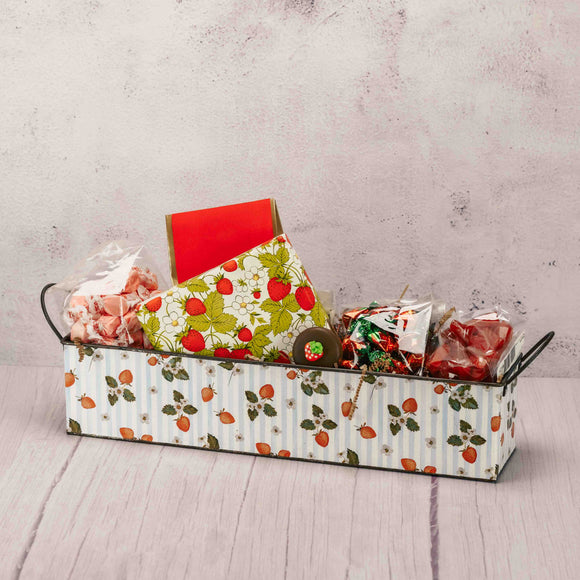 a small metal rectangle tin that is covered in strawberries is filled with sweet treats