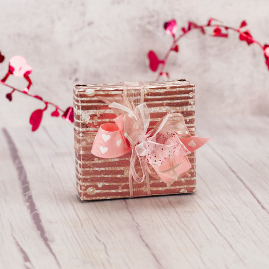 a sampler box of assorted chocolates is wrapped in pink paper with a bow on top