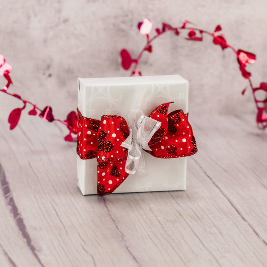 a sampler box of assorted chocolates is wrapped and tied with a stunning red bow