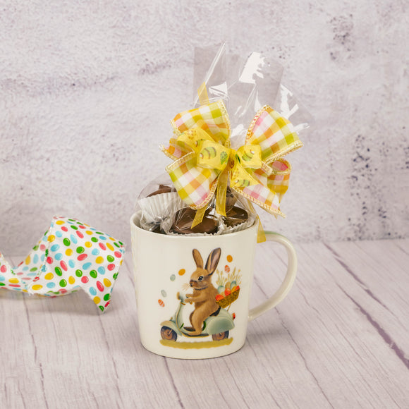 a half pound of assorted milk chocolates is packaged in this mug that has a bunny on a scooter.
