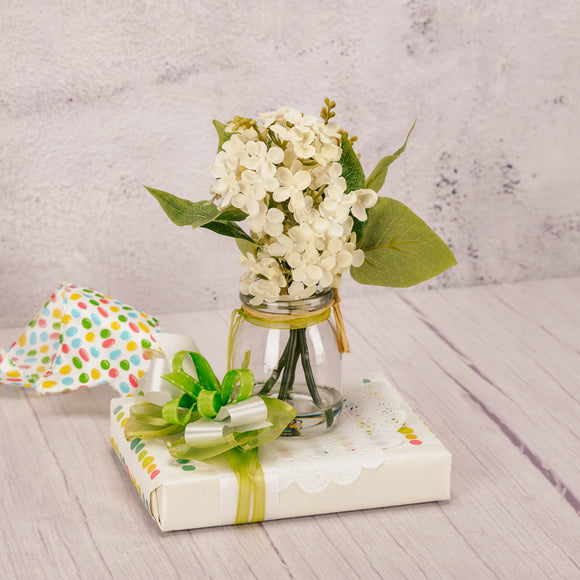 half pound box of assorted chocolates is wrapped and topped with a decorative glass jar holding white lilacs