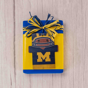 Michigan fans will enjoy hanging this wooden football player ornament for all to see who they cheer for on Saturdays! Placed on a half pound box of scrumptious Assorted Chocolates, this is sure to please any Wolverine fans! Choose a milk chocolate assortment or a combination of milk and dark chocolates.
