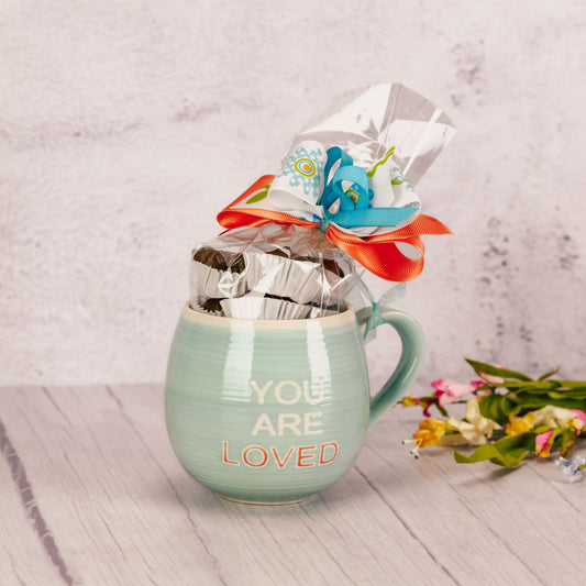 a half pound of our assorted milk chocolates is packaged in a teal mug that reads ' you are loved'.