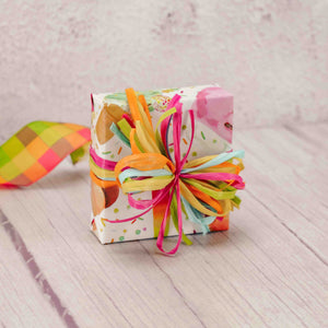 a sampler box of assorted chocolates is wrapped in ice cream paper and tied with a bright raffia ribbon bow