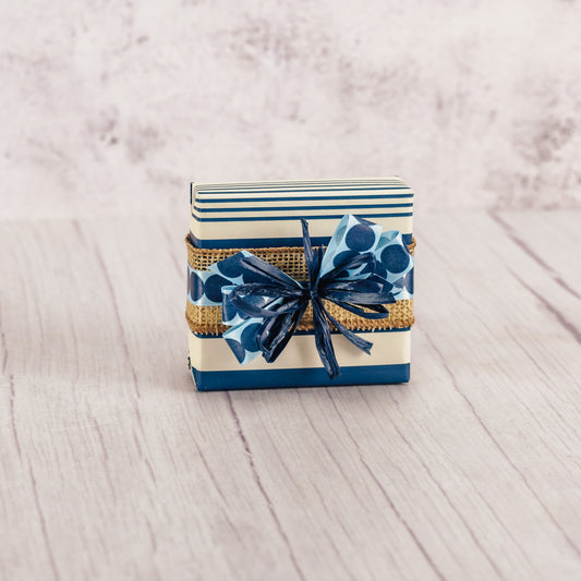 a sampler box of assorted chocolates wrapped in navy and white striped paper and tied with a handmade bow.
