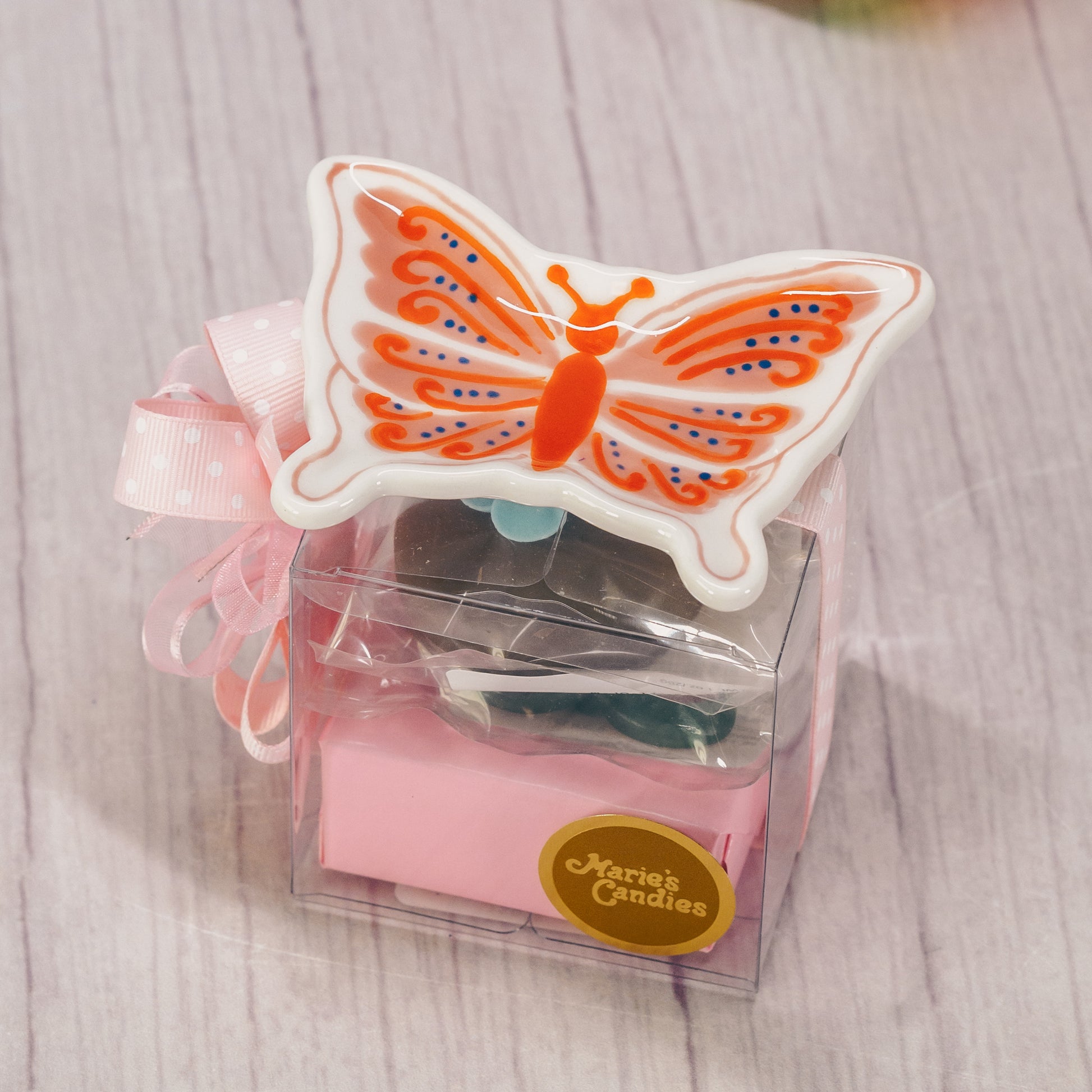A floral or butterfly trinket dish sits atop a clear cube box filled with sweet treats.