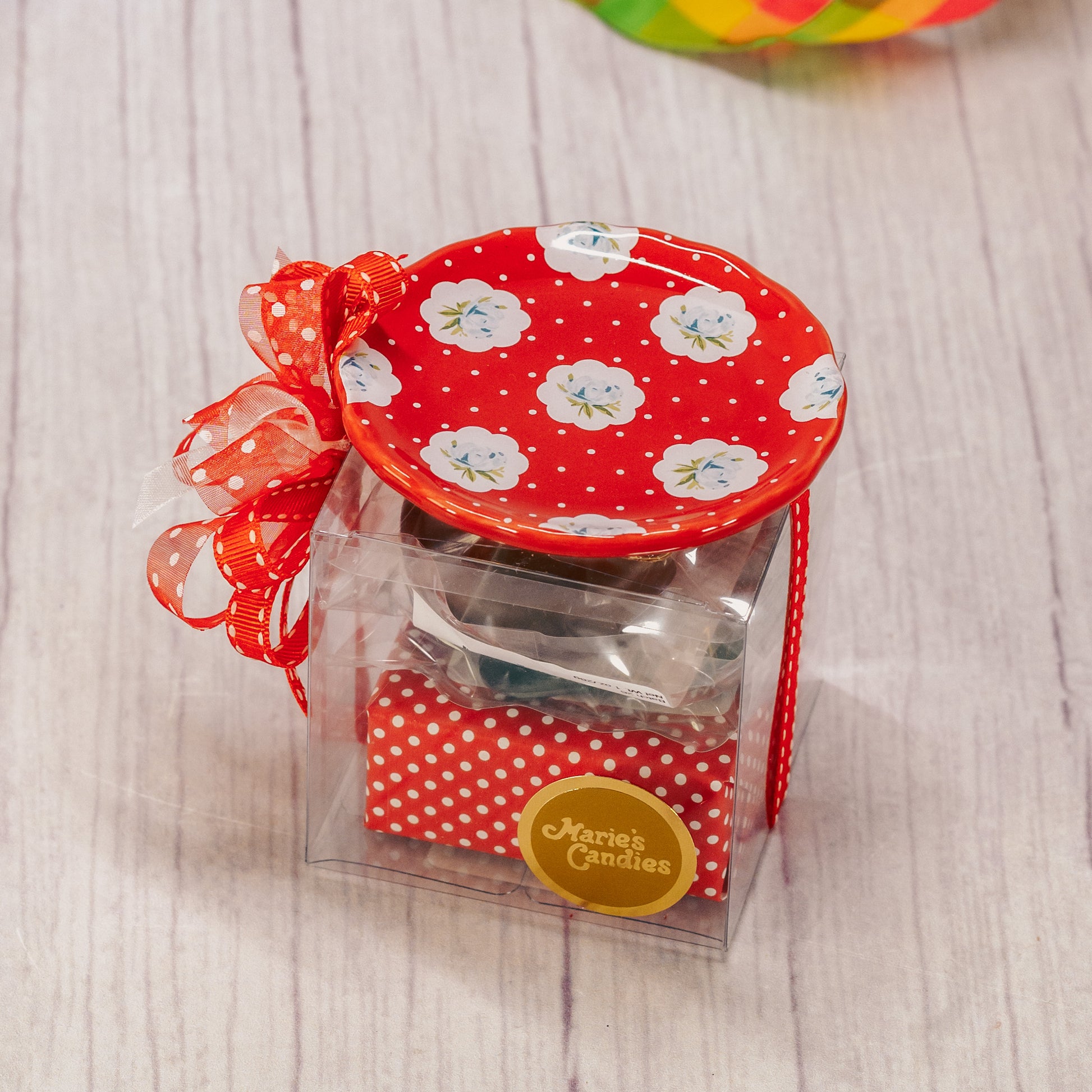 A floral or butterfly trinket dish sits atop a clear cube box filled with sweet treats.