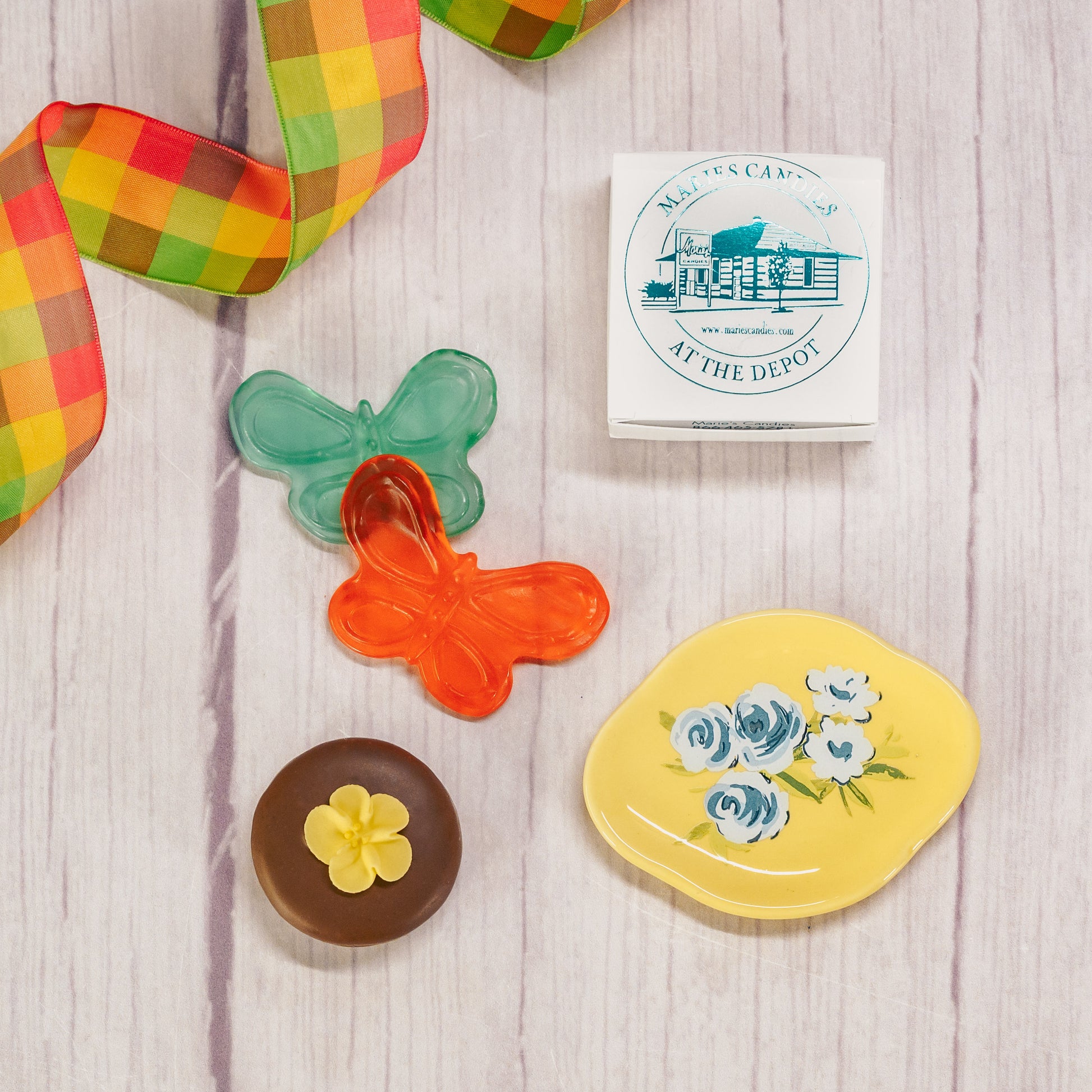 A floral or butterfly trinket dish sits atop a clear cube box filled with sweet treats.