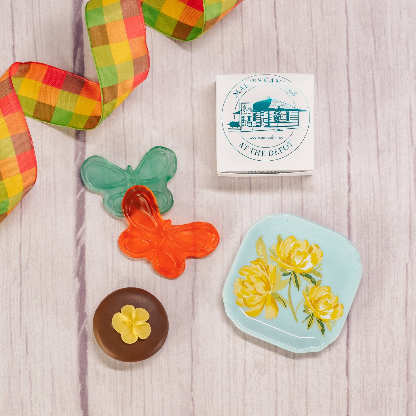 A floral or butterfly trinket dish sits atop a clear cube box filled with sweet treats.