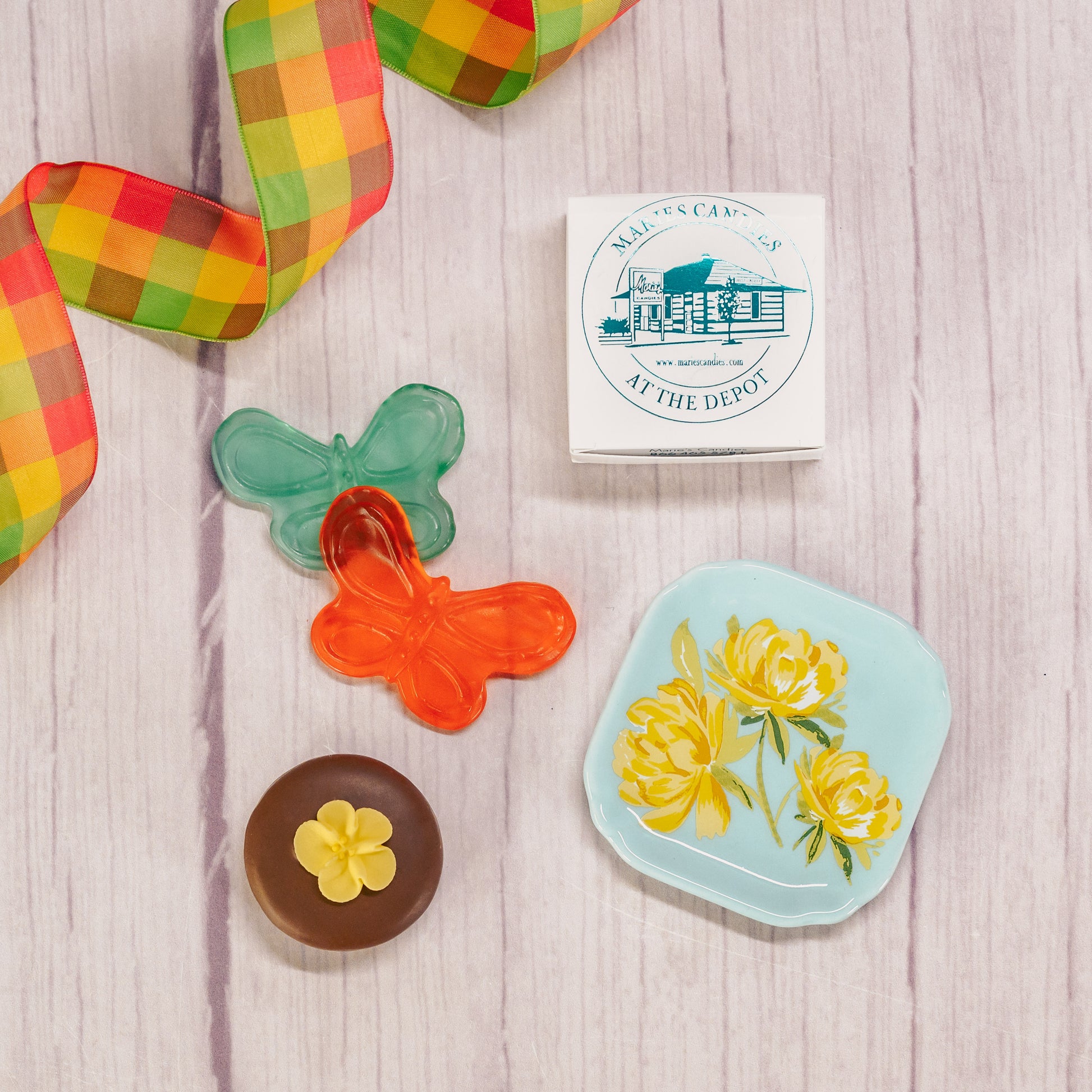 A floral or butterfly trinket dish sits atop a clear cube box filled with sweet treats.