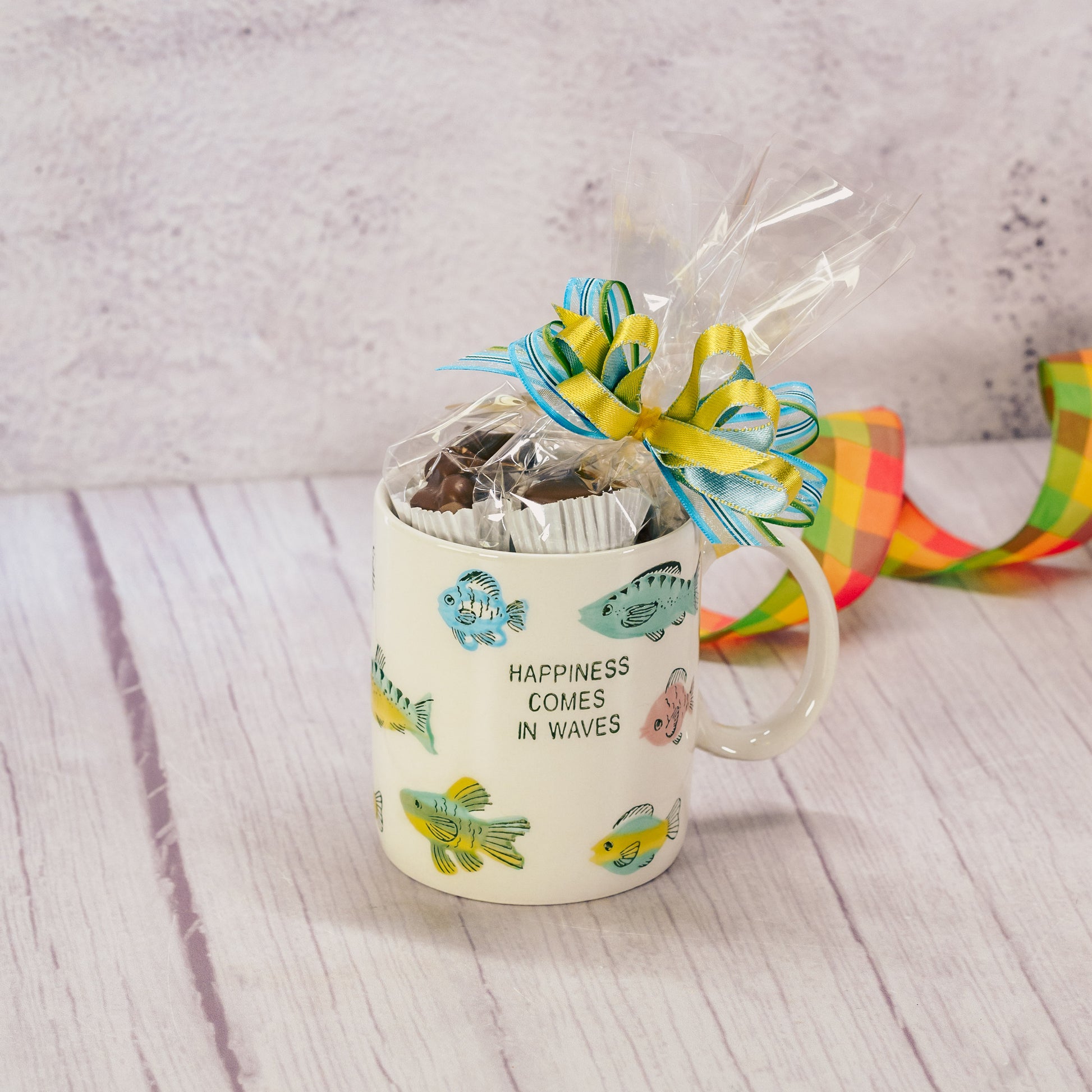 a mug that reads 'happiness comes in waves' with fish all over is filled with a half pound of our assorted milk assorted chocolates