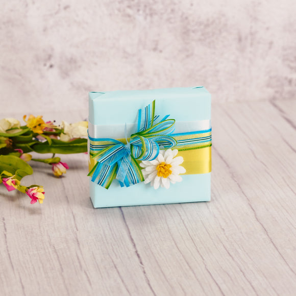 a sampler box of assorted chocolates is wrapped and topped with a small felt white daisy magnet