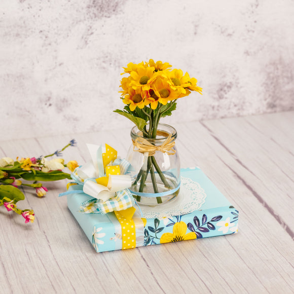 a half pound box of assorted chocolates is wrapped and topped with a decorative glass vase with yellow daisies