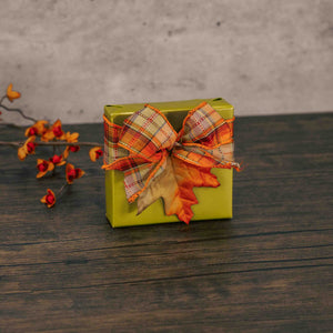 a sampler wrapped in fall green is topped with a fall plaid bow and a  decorative leaf