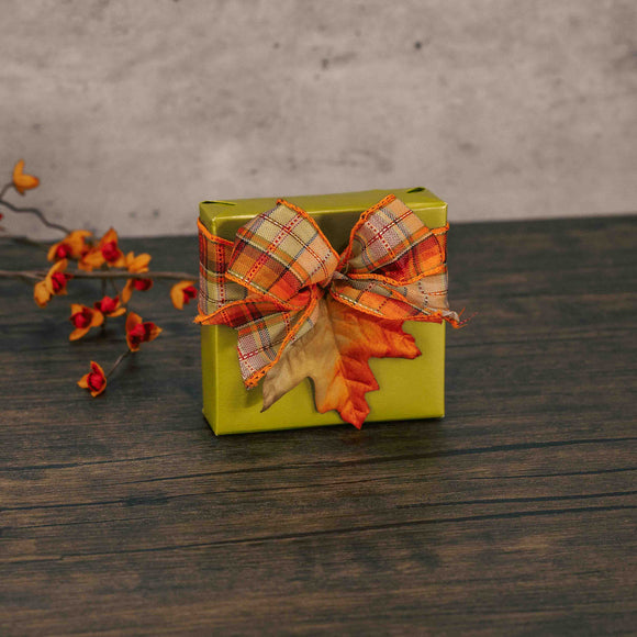 a sampler wrapped in fall green is topped with a fall plaid bow and a  decorative leaf