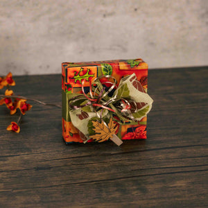 a sampler box of assorted chocolates is wrapped in fall paper and tied with a handmade bow with a mini wooden leaf clothes pin