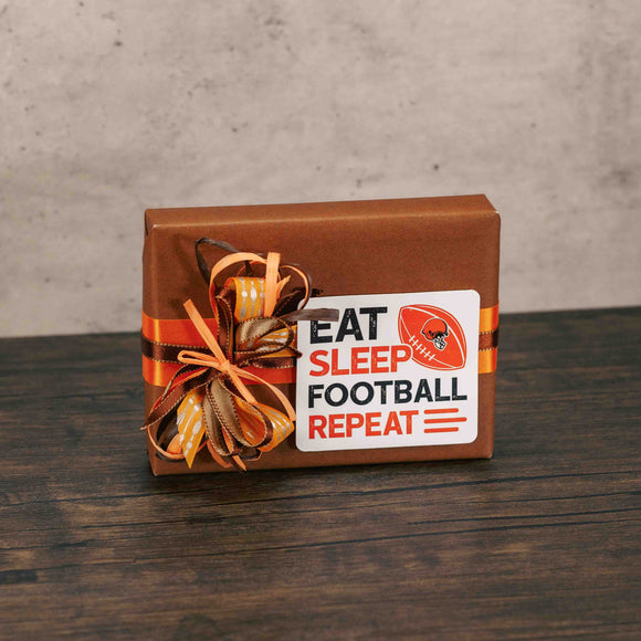 a half pound box of assorted chocolates is wrapped in brown and topped with a sticker that reads 'eat, sleep, football, repeat'