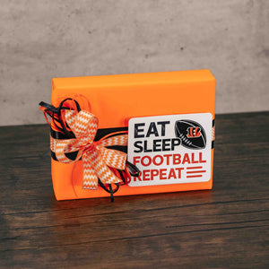 a half pound box of assorted chocolates is wrapped in orange paper and topped with a sticker that reads 'eat, sleep, football, repeart'