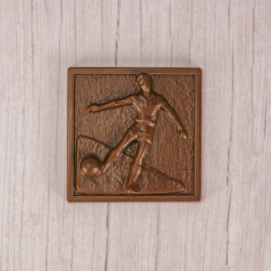 a square plaque of a soccer player kicking the ball in smooth milk chocolate