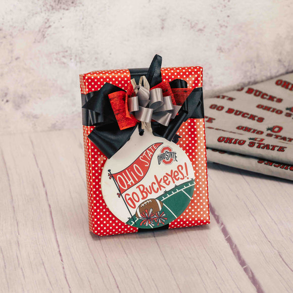 a half pound box of assorted chocolates is wrapped in red polka dot paper and topped with a round stone 'Go Buckeyes' ornament