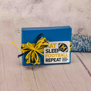 a half pound box of assorted chocolates is wrapped in blue and topped with a sticker that reads 'eat, sleep, football, repeat'