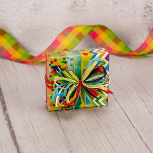a sampler box of assorted chocolates is wrapped in funfetti paper and tied with a colorful cheerful handmade bow.
