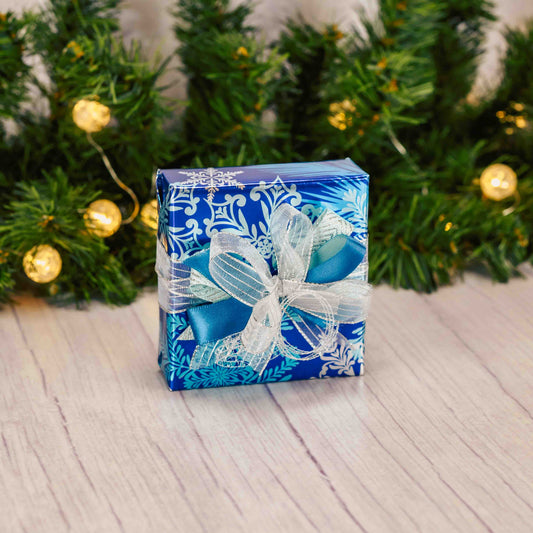 a sampler box of assorted chocolates is wrapped in blue shiny snowflake paper with a handmade bow on top.