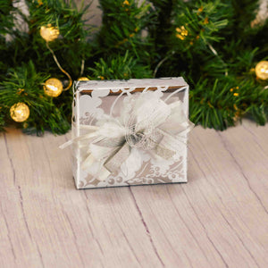 a sampler box of assorted chocolates is wrapped in silver holly paper and topped with a festive silver handmade bow