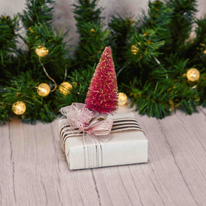 a sampler box of assorted chocolates is wrapped and topped with a pink bristle tree on top