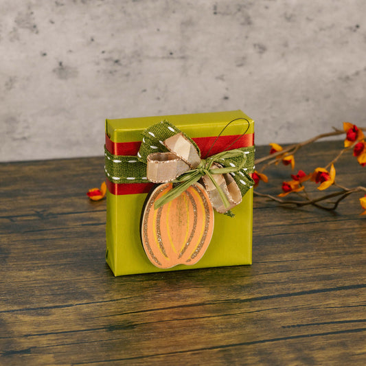 a sampler box of assorted chocolates is wrapped and tied with a sparkly wooden pumpkin ornament