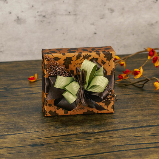 a sampler box of assorted chocolates is wrapped in fall leaf paper and topped with a festive handmade bow.