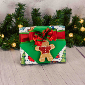 a half pound box of assorted chocolates is wrapped and topped with a flat wooden gingerbread man ornament