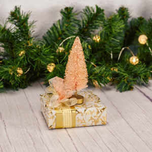 sample box of assorted chocolates is wrapped in gold and topped with a glittery coral bristle bottle tree